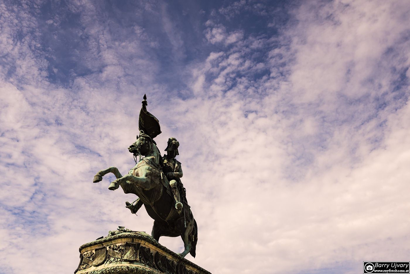 Ein bronzenes Reiterdenkmal von Erzherzog Carl auf einem Steinsockel vor einem dramatischen, leicht bewölkten Himmel in Wien.